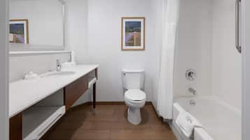A bathroom with a white sink, toilet, and shower. There is a framed picture on the wall.