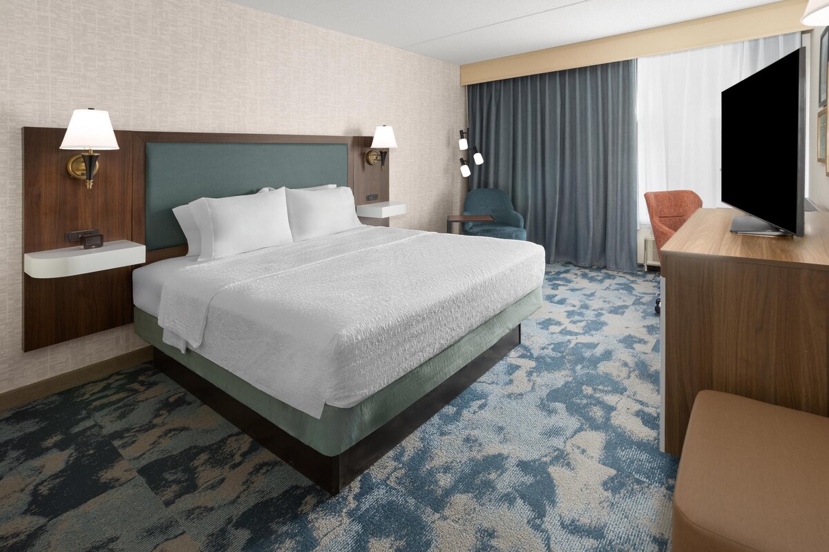 A hotel room with a large bed, two bedside tables with lamps, a flat-screen TV, a desk, and a chair.