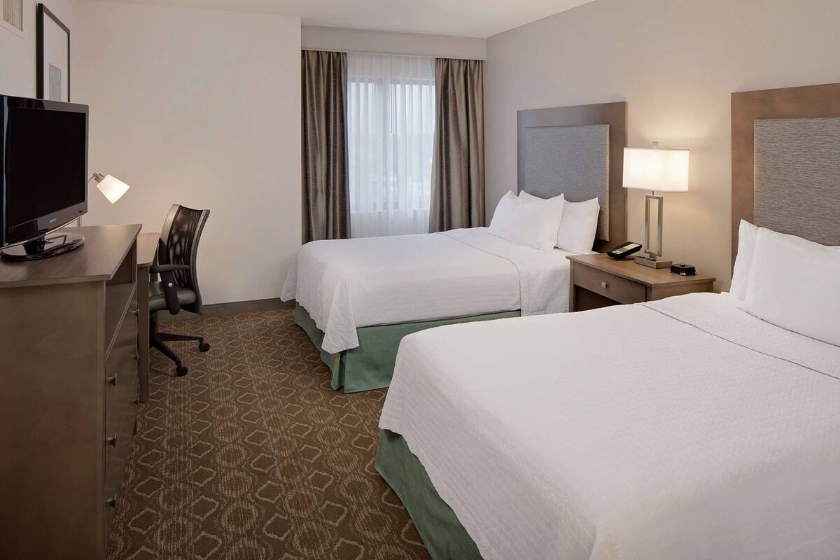 Een hotelkamer met twee bedden, een bureau met een computer, een stoel en een televisie.