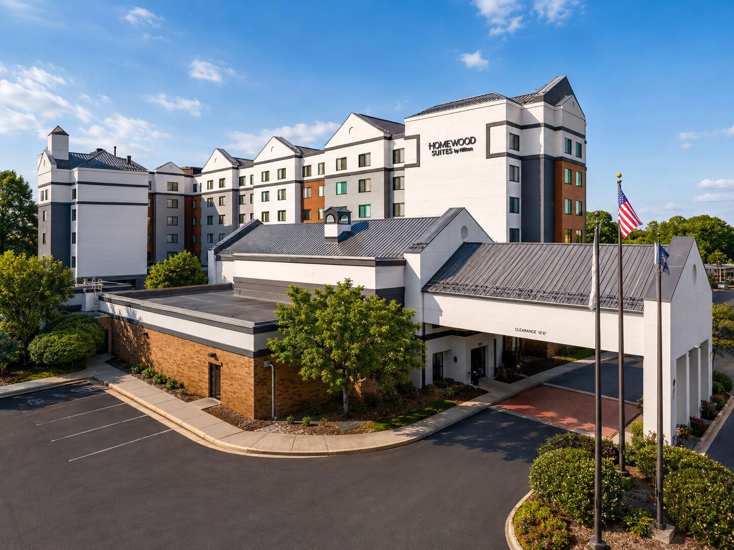 Hotel con diseño moderno, destacando un letrero grande de 'Homewood Suites by Hilton', un estacionamiento y un cielo despejado.