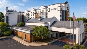 A hotel with a modern design, featuring a prominent 'Homewood Suites by Hilton' sign, a parking lot, and a clear sky.