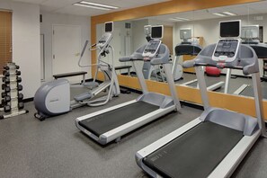 Une salle de sport équipée de tapis de course, de vélos elliptiques et de supports à poids.