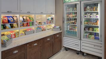 A kitchen area with snack shelves, a beverage fridge, and a coffee machine.