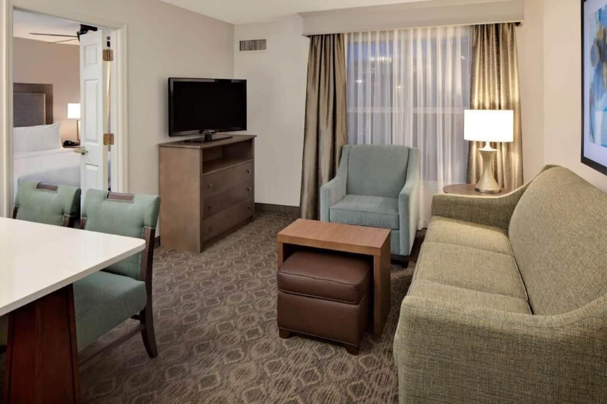 Een hotelkamer met een bed, een televisie, een bank, een stoel, een klein tafeltje en een lamp.