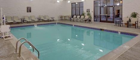 Une piscine intérieure dotée de chaises longues et de tables, un espace piscine dégagé et une porte de sortie.