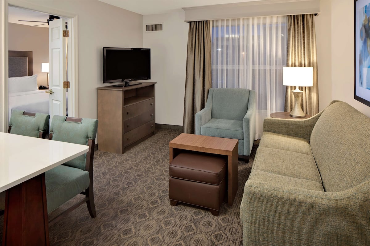 Een hotelkamer met een bed, een televisie, een bank, een stoel, een klein tafeltje en een lamp.