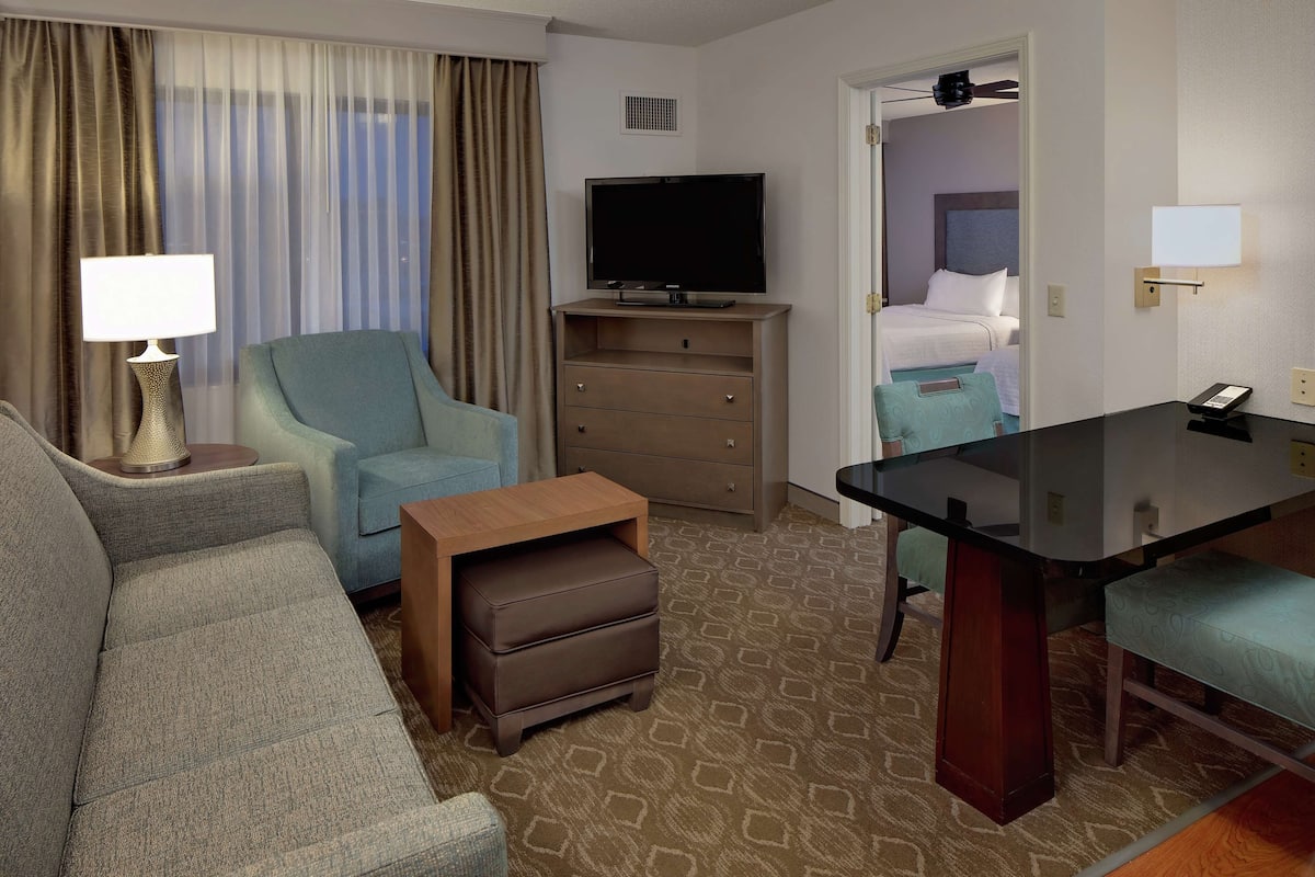 Een hotelkamer met een bank, een televisie, een bureau, een stoel, een dressoir en een bed.