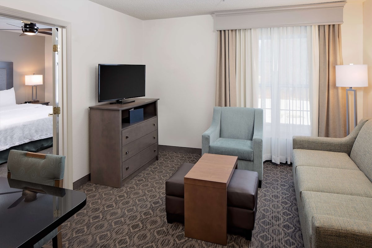 Hotelkamer met een bed, televisie, bureau, stoel, bank en raam met gordijnen.