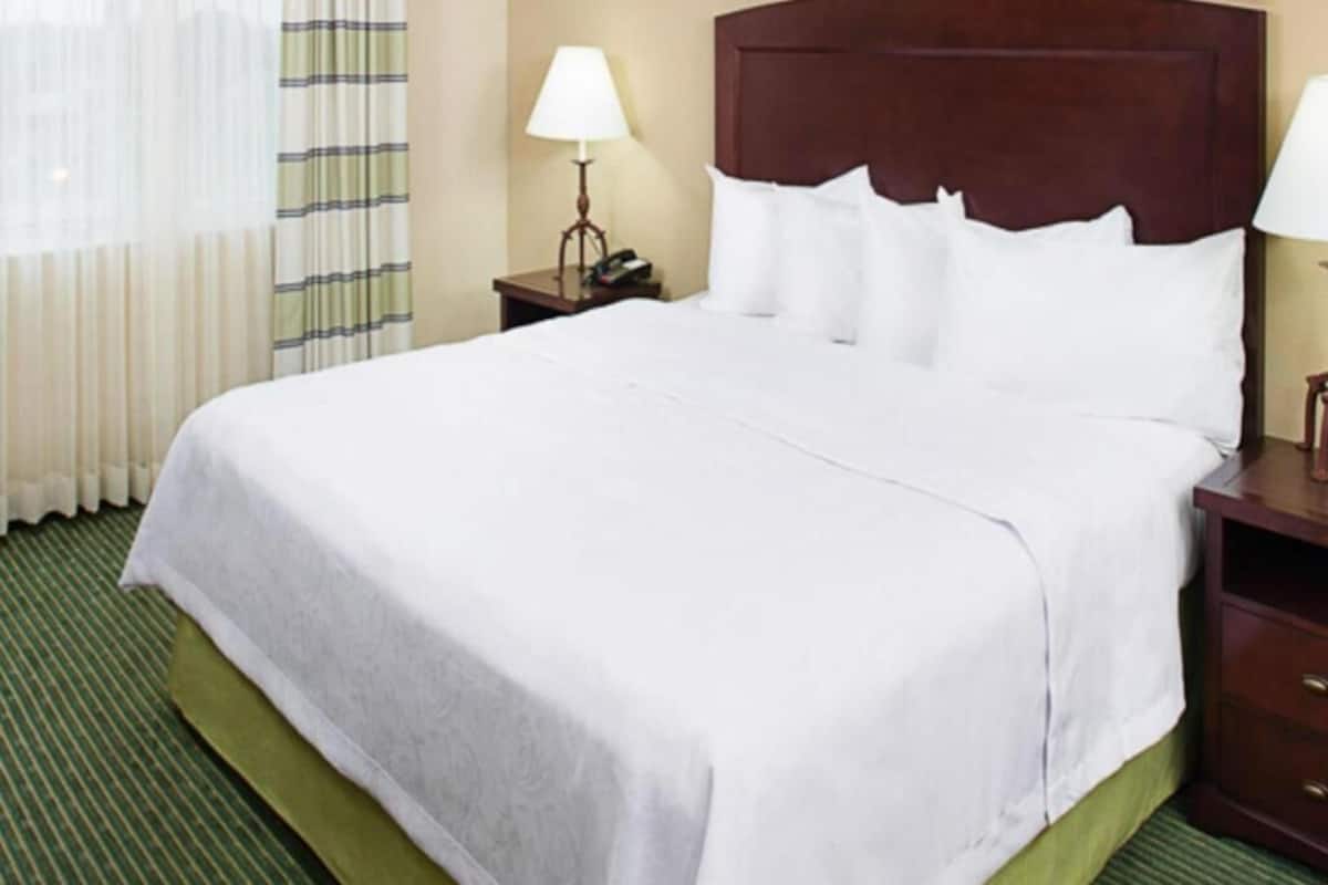 Een hotelkamer met een groot bed, een nachtkastje met lamp en een raam met gordijnen.