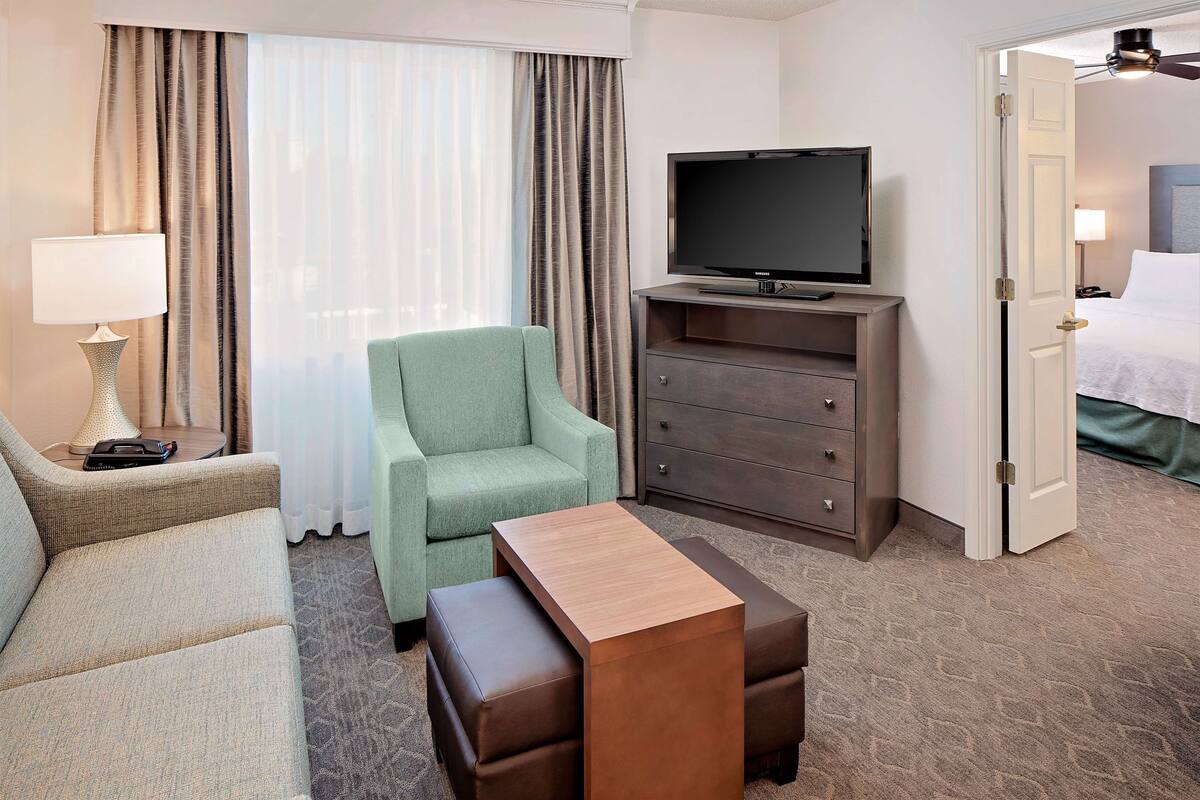 Een hotelkamer met een bank, een stoel, een televisie op een dressoir, een kast en een bed.