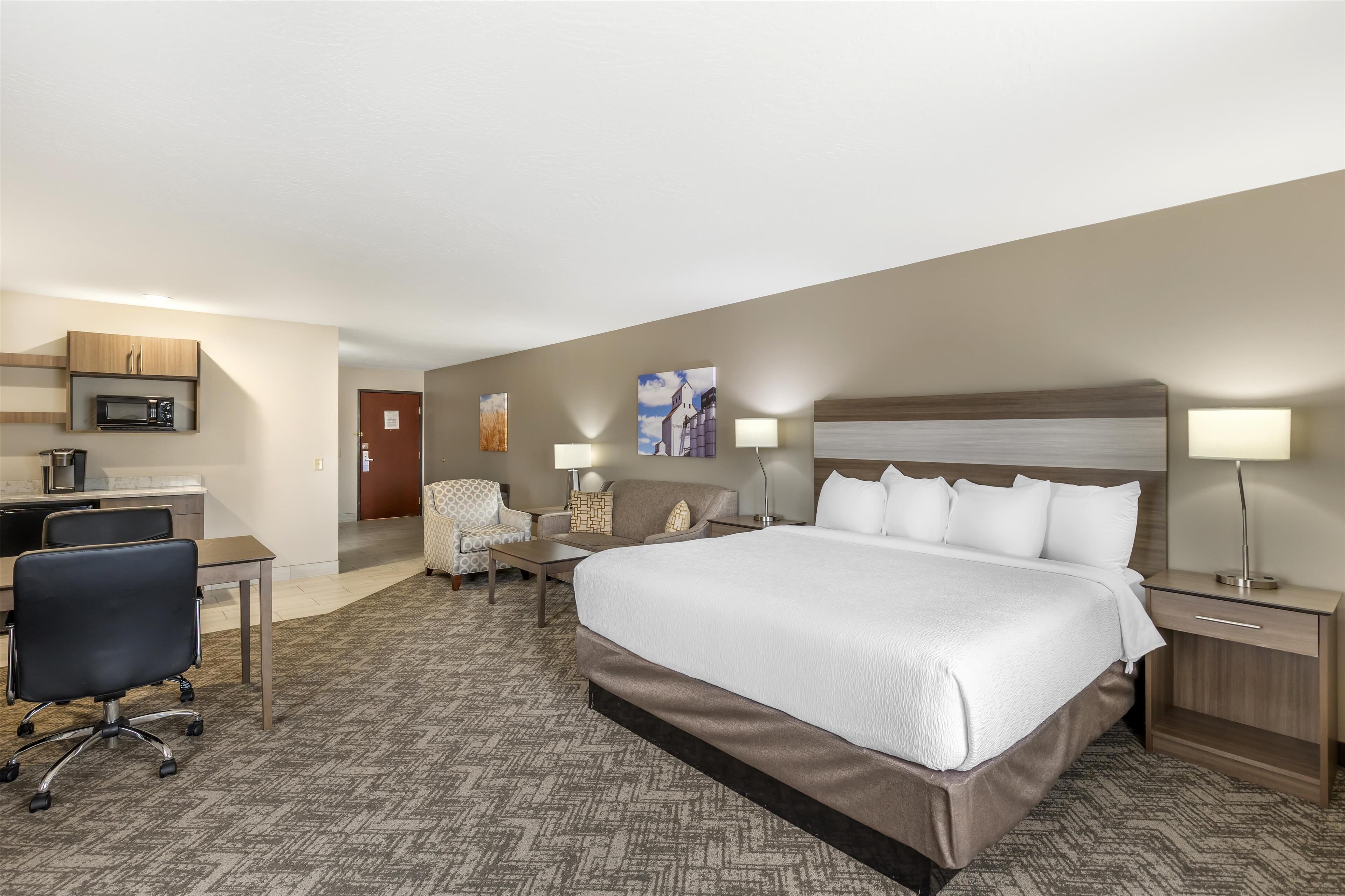 A hotel room with a large bed, a desk with a computer, a chair, a lamp, and a microwave.