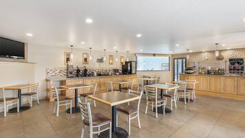 Un restaurante moderno con varias mesas y sillas, una zona de cocina y una pantalla grande en la pared.