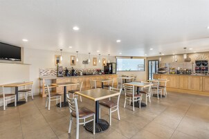 Un restaurante moderno con varias mesas y sillas, una zona de cocina y una pantalla grande en la pared.