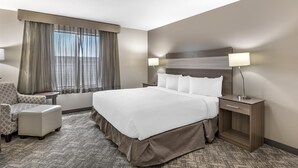 Une chambre d’hôtel avec un grand lit, deux tables de chevet, une chaise et une vue sur les toits de la ville par la fenêtre.