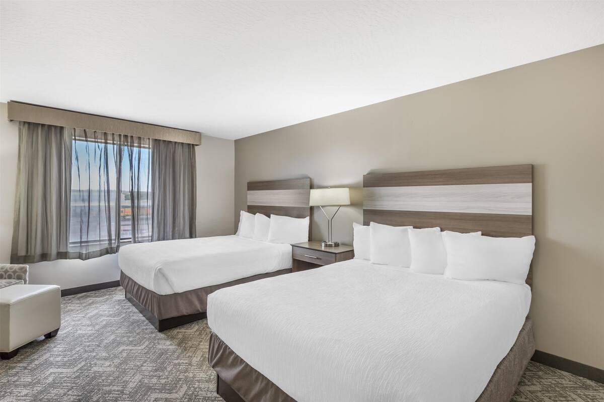 A hotel room with two beds, a desk, a chair, and a view of the city.