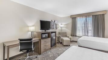 Ein Hotelzimmer mit Bett, Schreibtisch, Stuhl, Fernseher und einem kleinen Tisch mit Lampe.