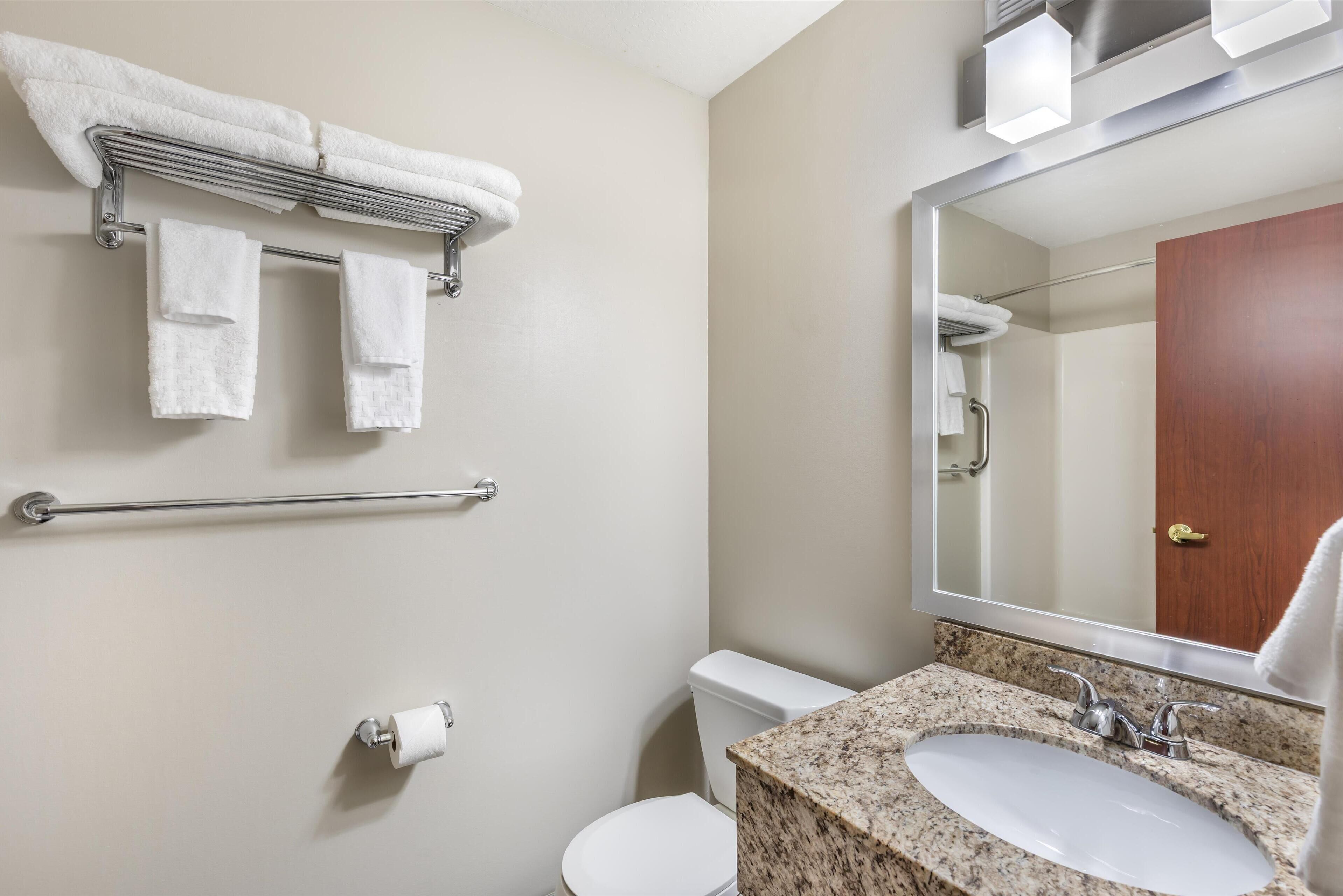 A bathroom with a white sink, a mirror, a towel rack with towels, a toilet, and a handrail.