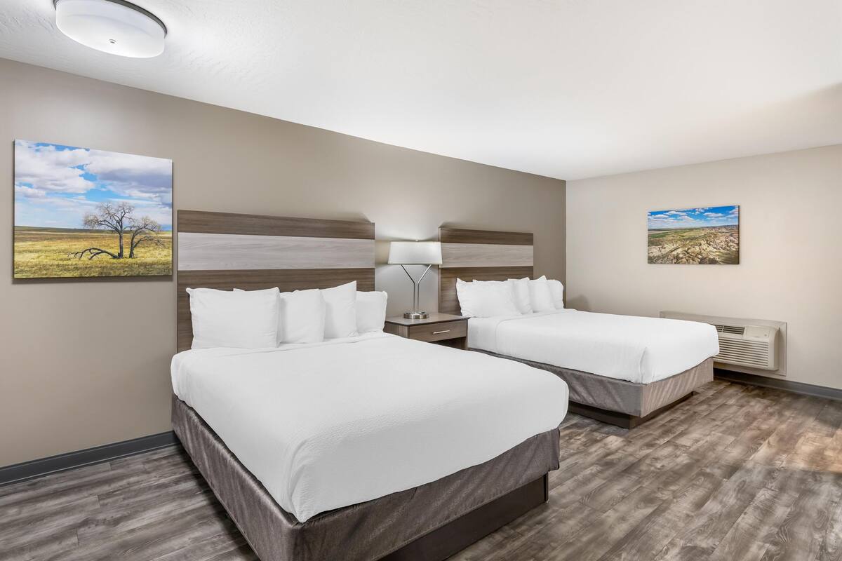 A hotel room with two beds, a nightstand, a lamp, and two framed pictures on the walls.