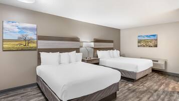 A hotel room with two beds, a nightstand, a lamp, and two framed pictures on the walls.