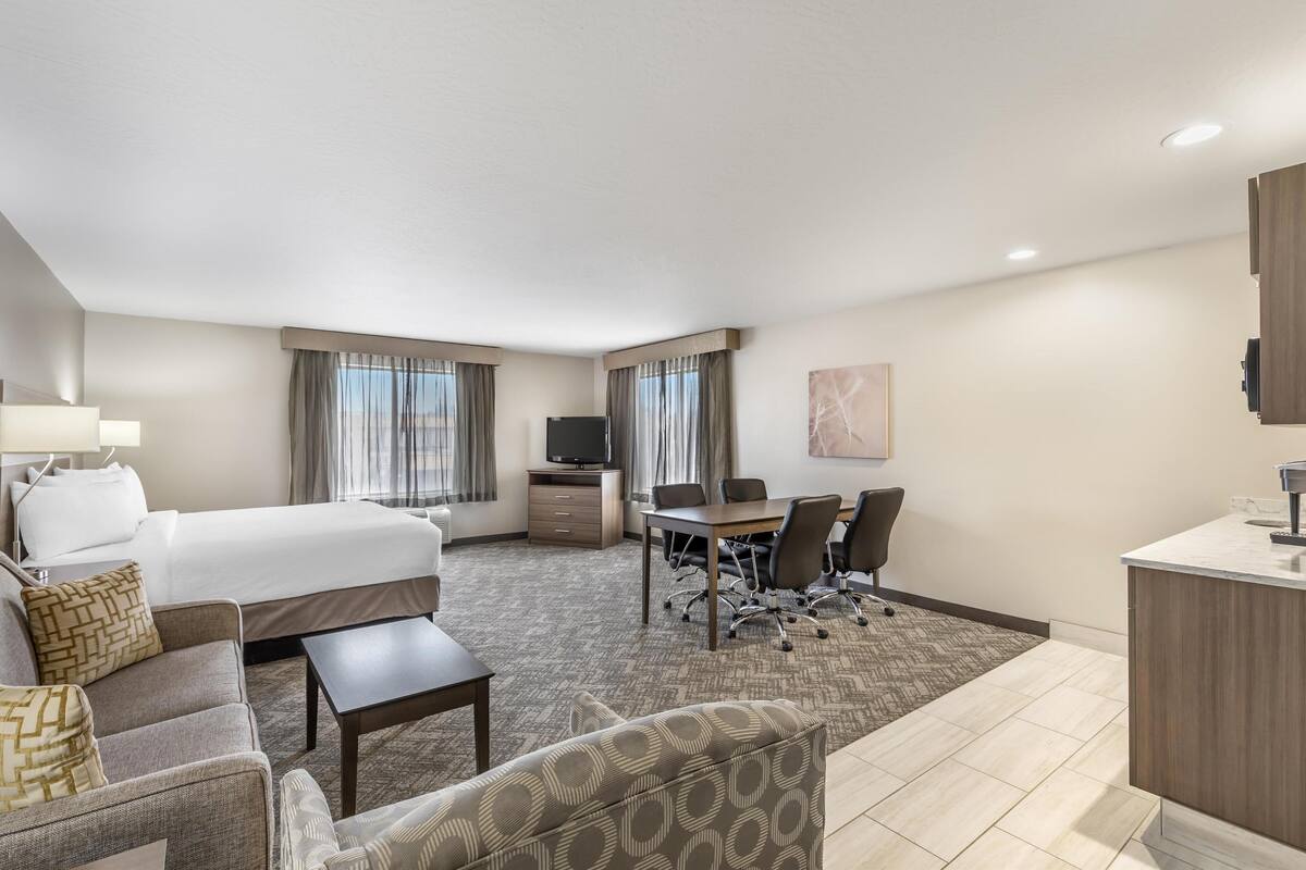 A hotel room with a large bed, a desk, a chair, a sofa, and a TV.