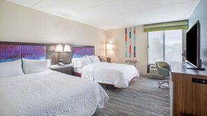 A hotel room with two beds, a desk with a computer, a TV, and a window with a view.