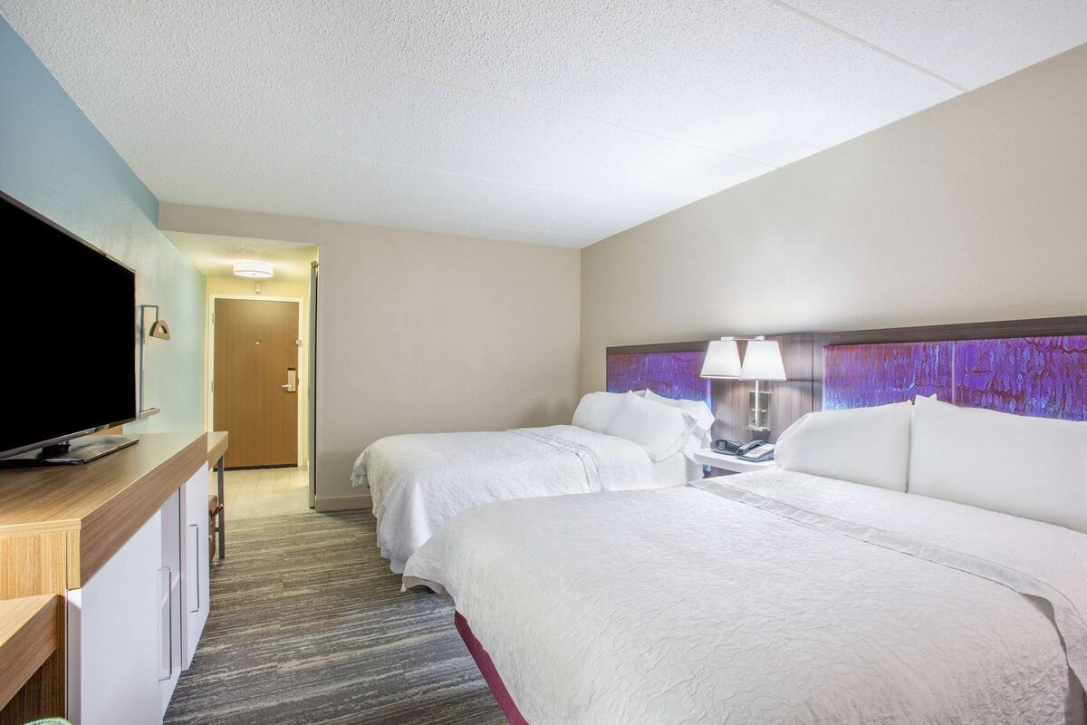 A hotel room with two beds, a TV, a desk, and a lamp.