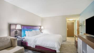 A hotel room with a bed, a desk, a chair, a television, and a door leading to another room.