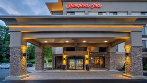 A hotel entrance with a modern design, featuring a prominent sign, stone pillars, and a covered walkway.