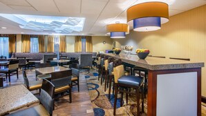 A hotel dining area with multiple tables and chairs, a central bar, and a ceiling with skylights.