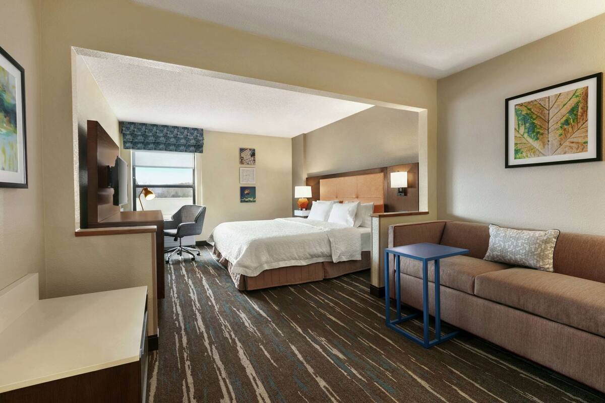 A hotel room with a bed, a desk, a chair, a sofa, and a small table.