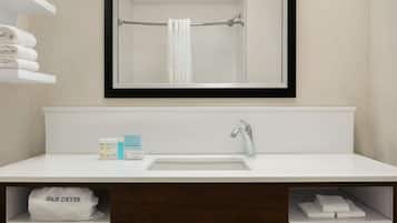 A modern bathroom with a white sink, a mirror, and a towel rack. There are towels on the rack and a hair dryer in a cabinet.