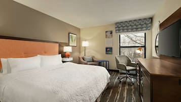 A hotel room with a large bed, a desk, a chair, a TV, and a window with a view.