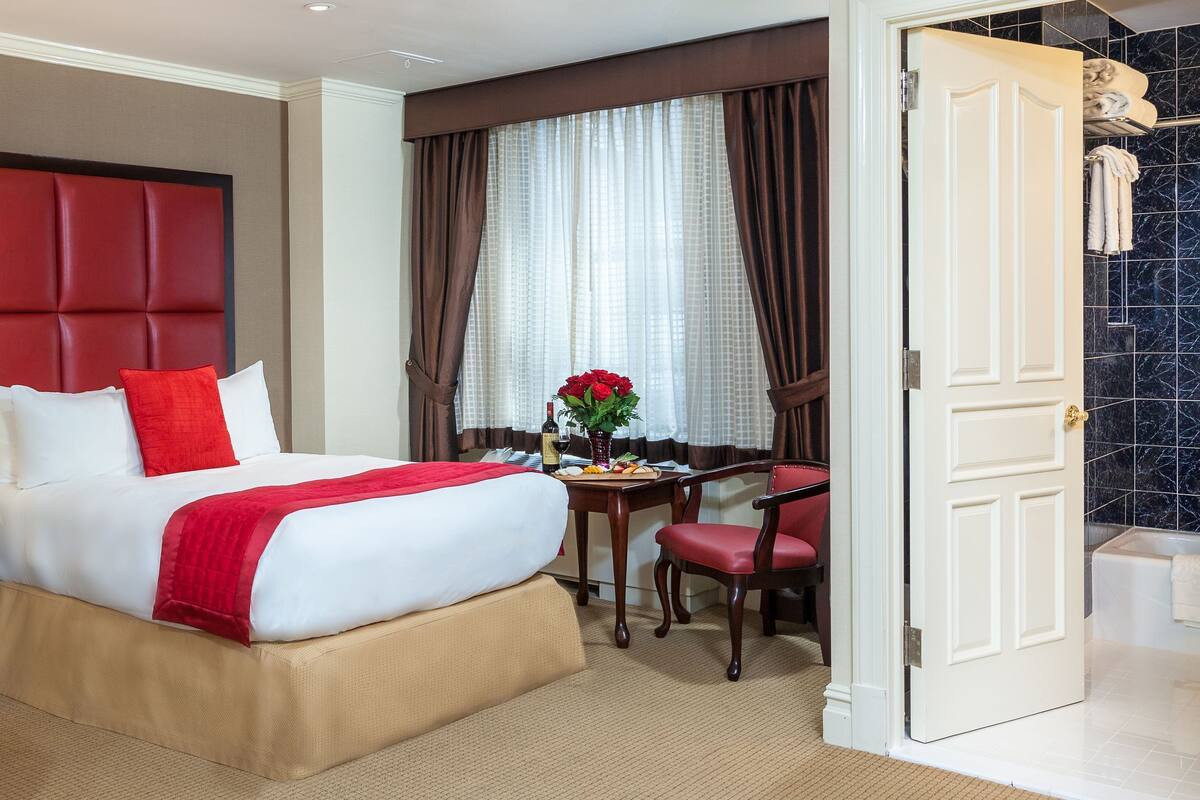 Quarto de hotel com duas camas, uma escrivaninha, uma cadeira, um abajur e um banheiro visível por uma porta aberta.