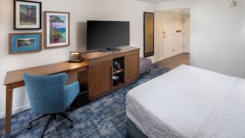 Una habitación de hotel con una cama, un escritorio con televisor, una silla y cuadros en la pared.