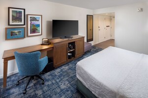 Una habitación de hotel con una cama, un escritorio con televisor, una silla y cuadros en la pared.