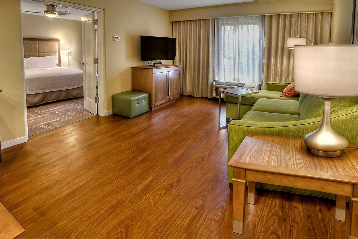 Una habitación de hotel con una cama, un televisor, un sofá verde, una mesa de madera y una lámpara.