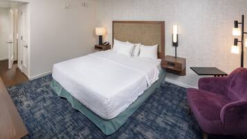 A hotel room with a large bed, two bedside tables with lamps, a purple armchair, and a blue carpet.