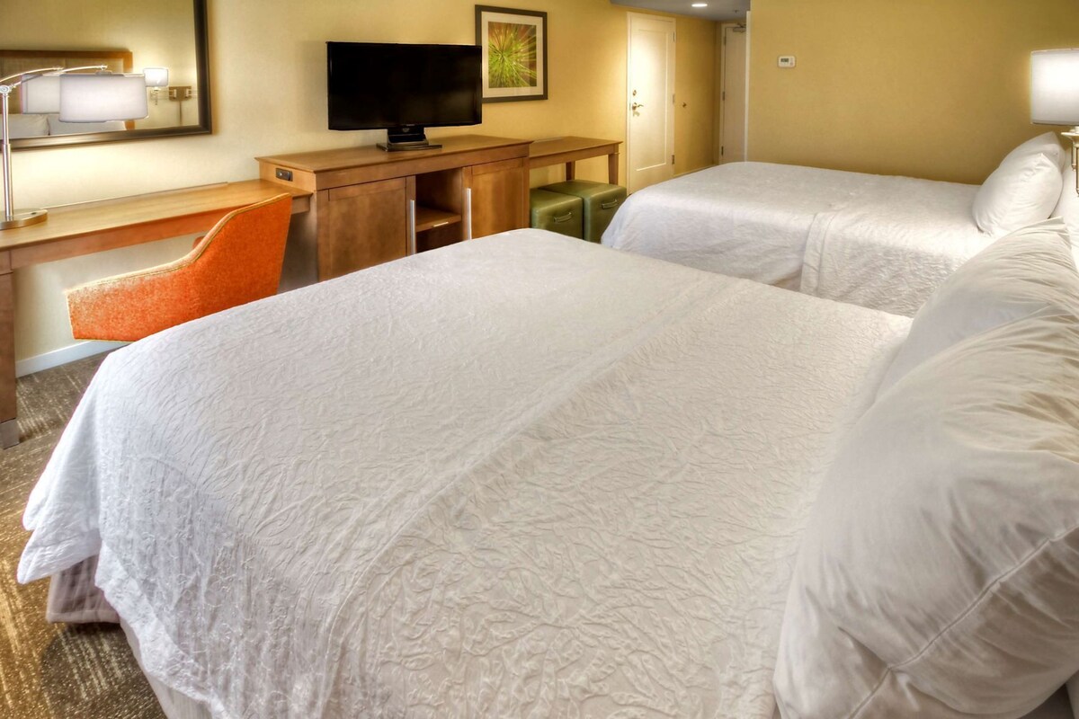 Une chambre d’hôtel avec deux lits, un bureau avec une télévision et une chaise.