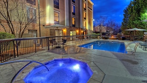 A heated outdoor pool area with a hot tub, lounge chairs, and a patio table.