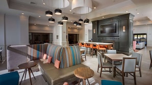 A modern hotel lobby with a seating area, a bar, and a large TV screen.