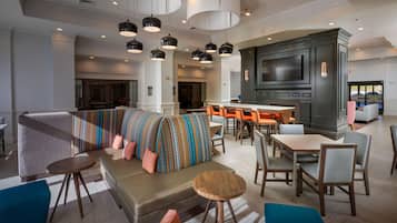 En moderne hotellobby med et siddeområde, en bar og et fjernsyn ophængt på væggen.