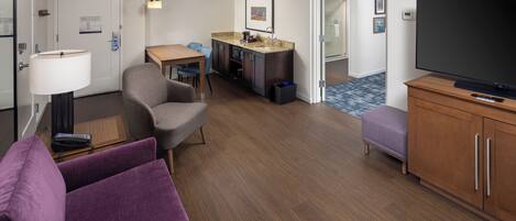 Una habitación de hotel moderna con sala de estar, kitchenette, televisor y baño.