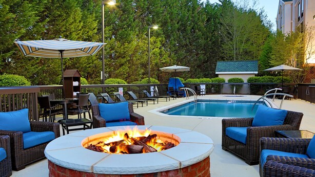 An outdoor pool area with lounge chairs, a fire pit, and umbrellas.