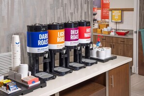 Estación de café con cuatro dispensadores etiquetados como tostado oscuro, tostado claro, descafeinado y agua caliente.