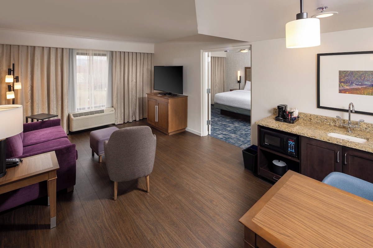Une chambre d’hôtel équipée d’un lit, d’une télévision, d’un bureau, d’une chaise, d’une petite table, d’une kitchenette et d’une salle de bain.