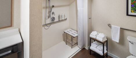 A bathroom with a shower, toilet, and a shelf with towels.