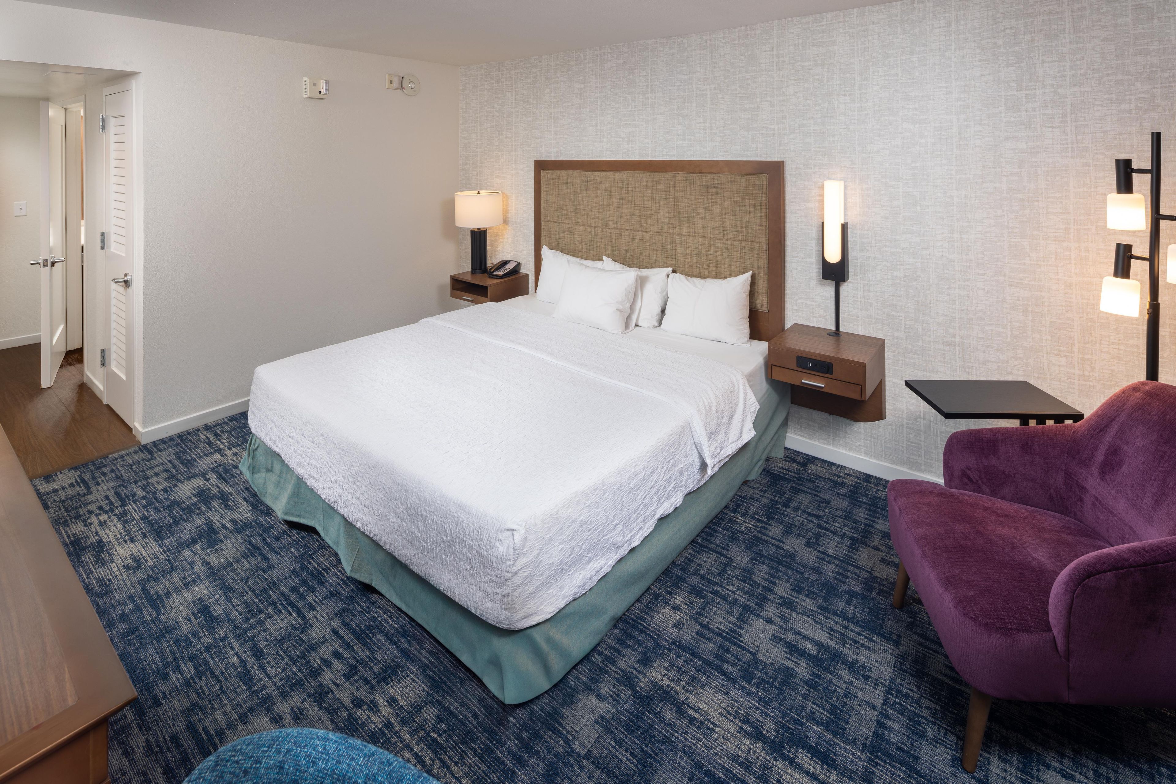 A hotel room with a large bed, bedside tables, a desk, a chair, and a patterned carpet.