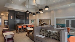A modern hotel lobby with a seating area, a kitchen, and a large TV screen.
