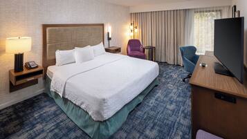 Una habitación de hotel con una cama grande, un escritorio con televisor, una silla, una lámpara y un teléfono en la mesita de noche.