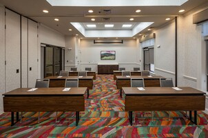 Un salón de conferencias con varias mesas y sillas, una alfombra colorida y un techo con tragaluces.